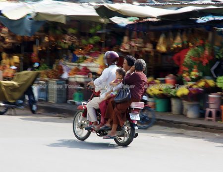 An overladen motorcycle bears a family past one of Phnom Penh's many markets.